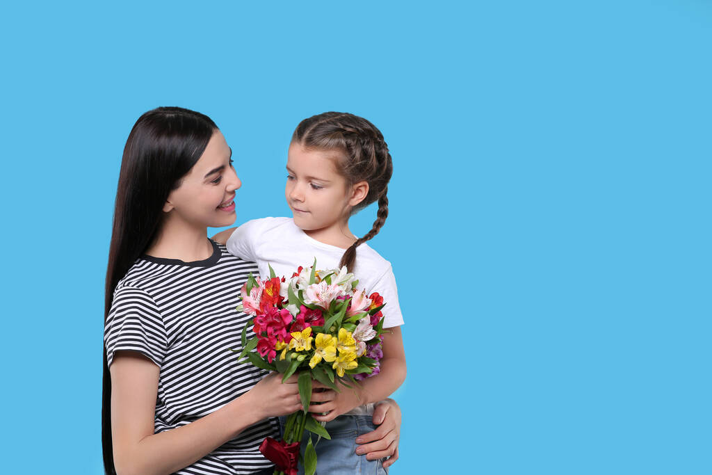 Szczęśliwa kobieta z córką i bukiet pięknych kwiatów na jasnoniebieskim tle, miejsce na tekst. Święto Dnia Matki - Zdjęcie, obraz