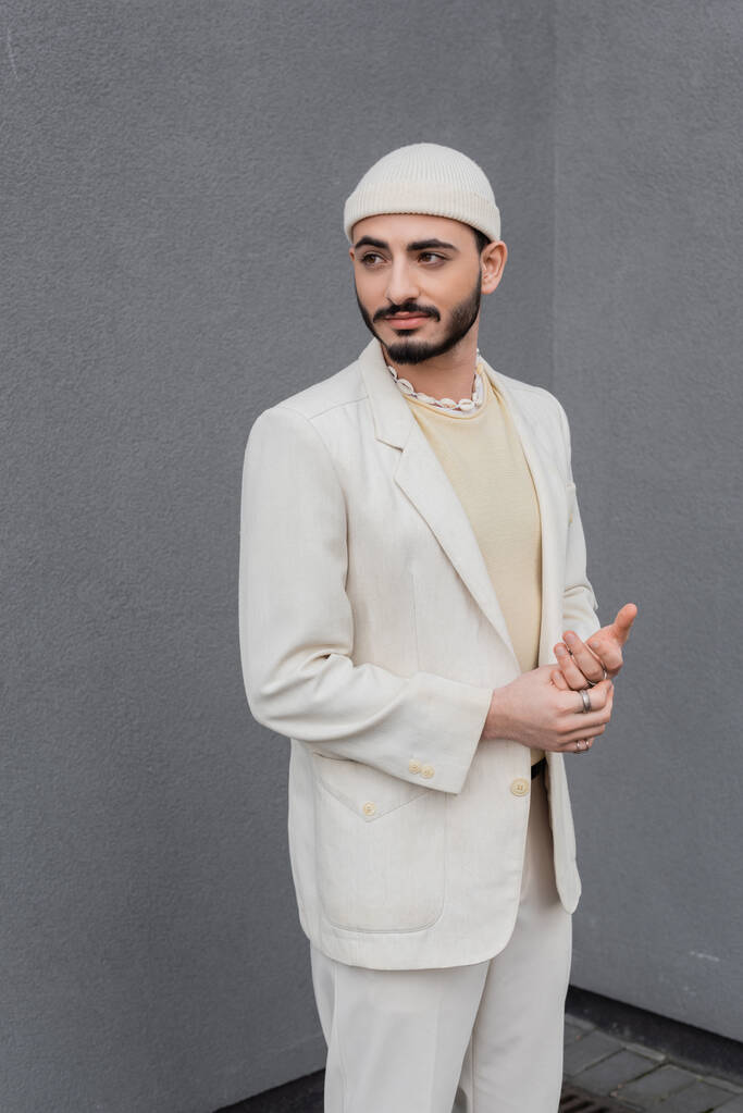 Trendy gay uomo in cappello e beige vestito in piedi vicino edificio all'aperto  - Foto, immagini