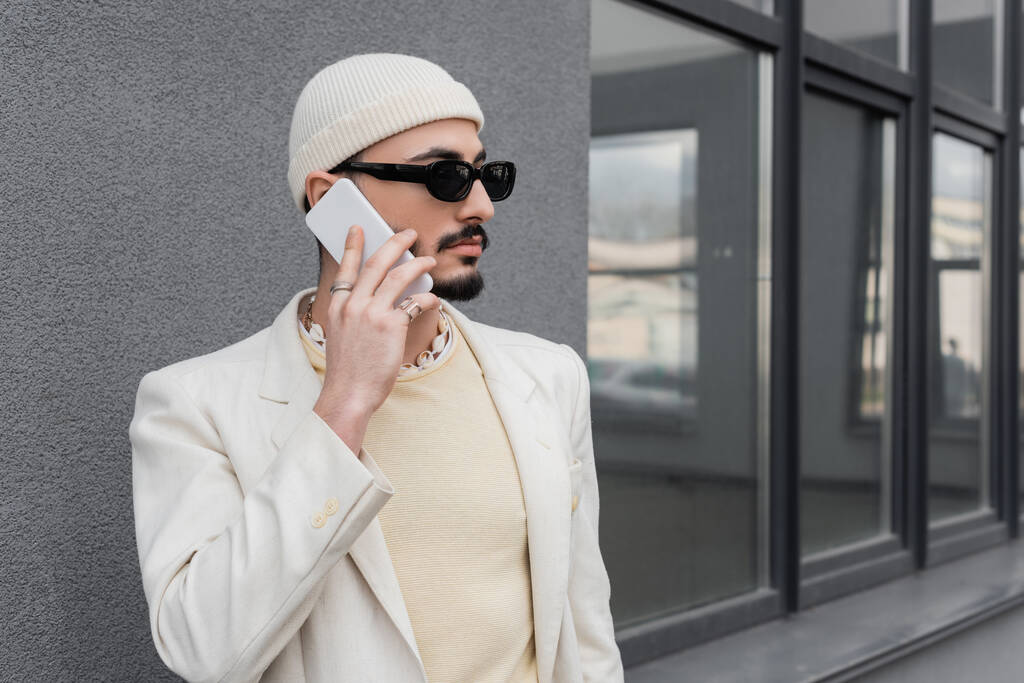 Trendy homosexuelle Mann mit Sonnenbrille spricht auf Handy auf der Straße in der Stadt  - Foto, Bild