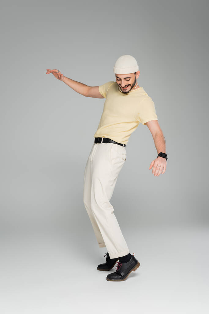 Täysi pituus trendikäs ja iloinen homo mies poseeraa harmaalla taustalla  - Valokuva, kuva