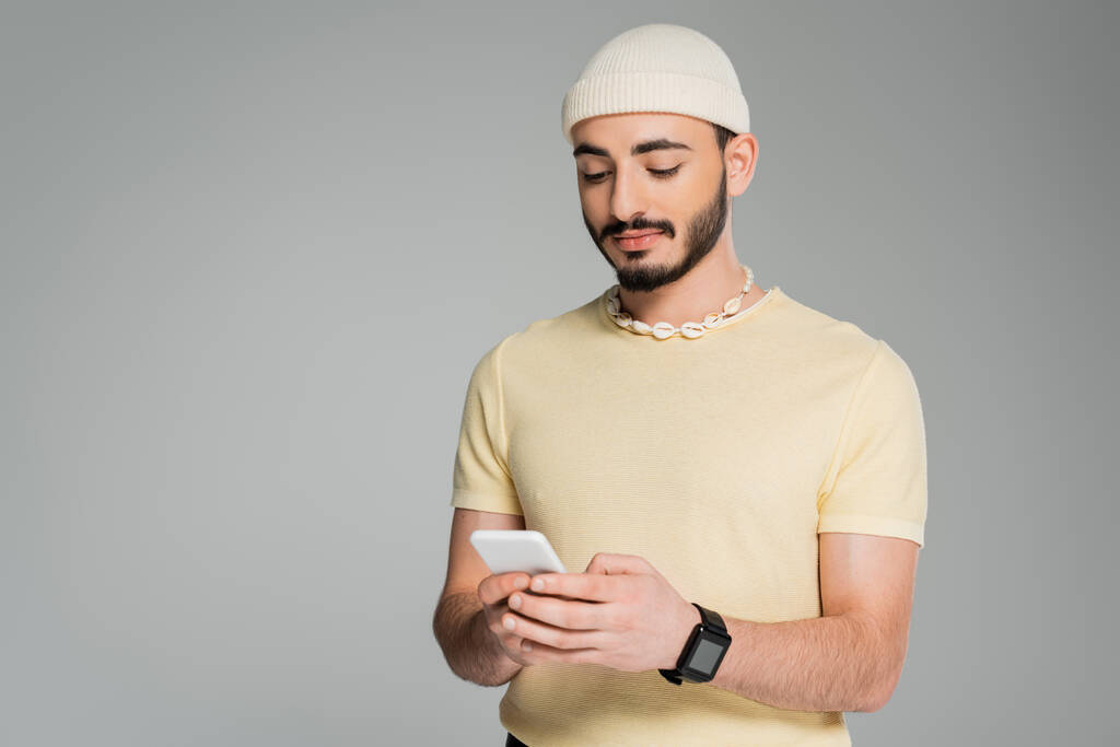 Модний гей-чоловік у капелюсі використовує мобільний телефон ізольований на сірому
   - Фото, зображення