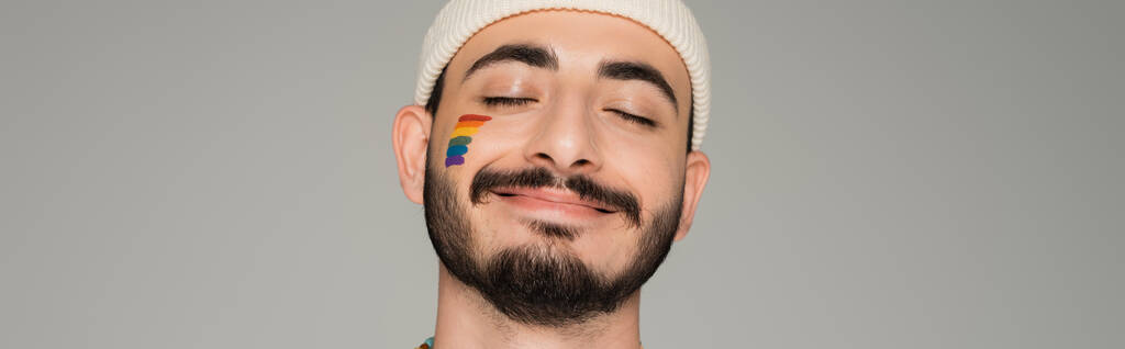 Mosolygó homoszexuális férfi kalapban lgbt zászlóval az arcán elszigetelt szürke, banner  - Fotó, kép