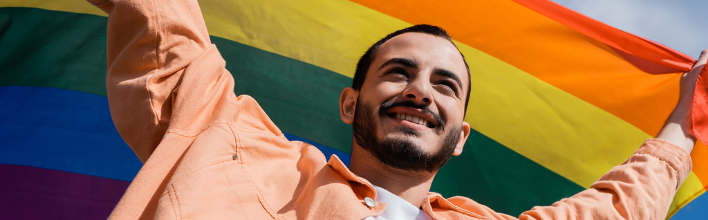 Baixo ângulo vista de alegre homossexual homem segurando lgbt bandeira ao ar livre, banner  - Foto, Imagem