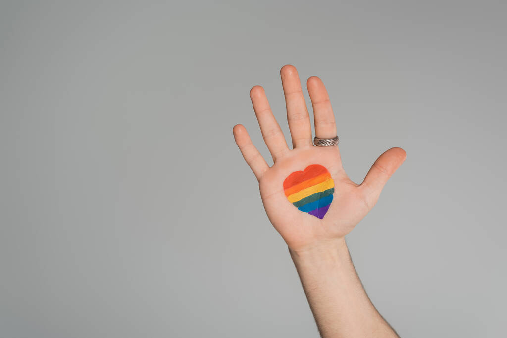 Cropped view of gay man with lgbt flag in heart shape on hand isolated on grey, Journée internationale contre l'homophobie - Photo, image