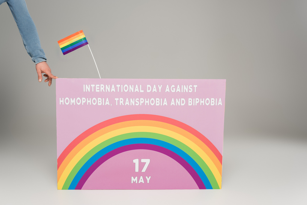 Vista ritagliata dell'uomo gay vicino al cartello con la Giornata internazionale contro omofobia, transfobia e bifobia lettering sul grigio  - Foto, immagini