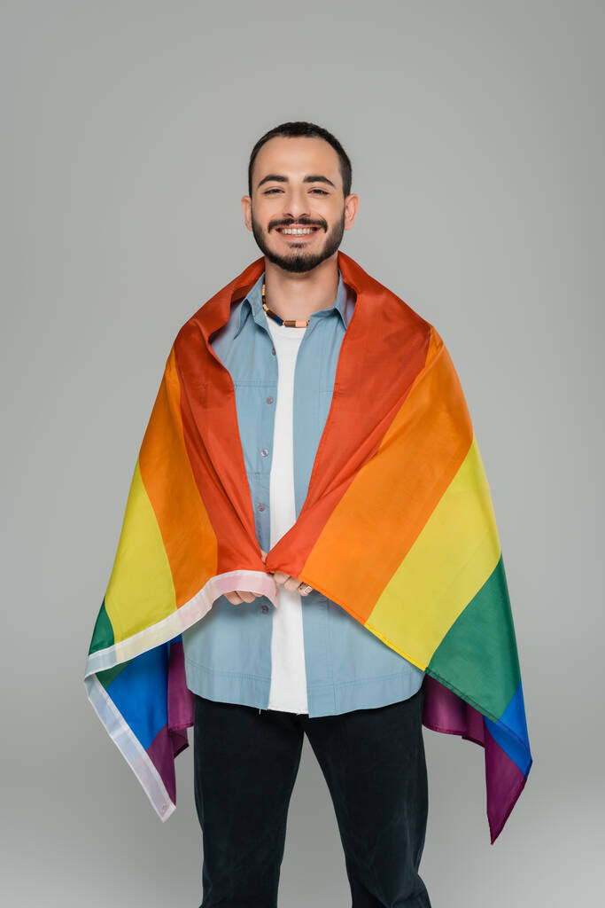 wesoły gej człowiek patrząc w aparat i trzymając lgbt flaga izolowane na szary Międzynarodowy Dzień przeciw homofobii - Zdjęcie, obraz