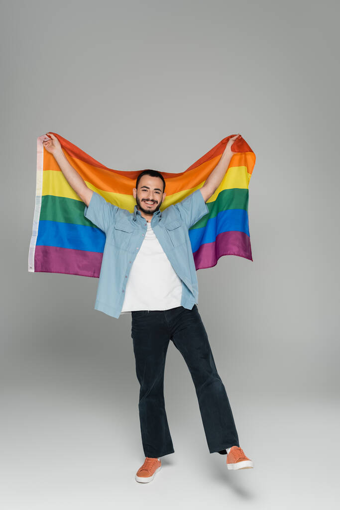 Pleine longueur de l'homme homosexuel positif tenant drapeau lgbt sur fond gris  - Photo, image