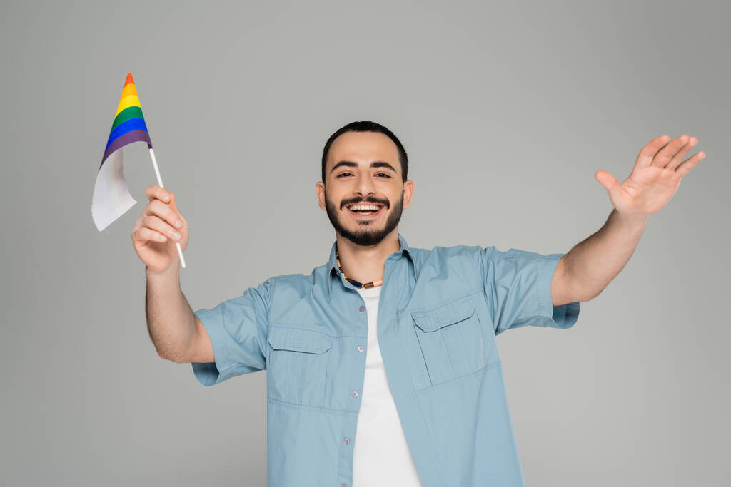 Θετικός και γενειοφόρος ομοφυλόφιλος άνδρας με σημαία Igbt απομονωμένη την γκρίζα, διεθνή ημέρα ομοφοβίας - Φωτογραφία, εικόνα