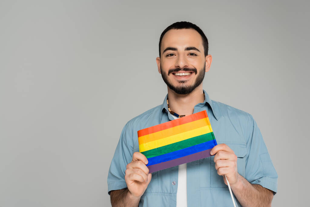 Retrato de alegre gay hombre en camisa celebración lgbt bandera aislado en gris   - Foto, imagen