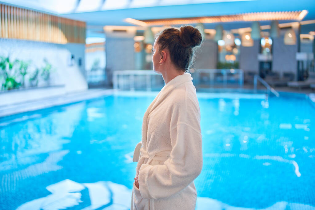 Unbekümmert heitere Frau im Bademantel chillt und entspannt allein am Pool im Wellness-Center. Geistesgesundheit und Urlaub - Foto, Bild