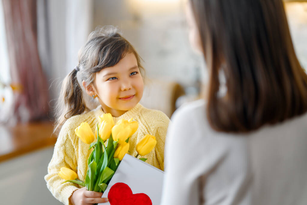 Szczęśliwego Dnia Matki. Dziecko córka gratuluje matce i daje jej bukiet kwiatów. - Zdjęcie, obraz