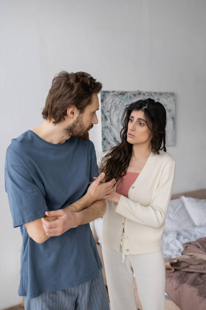 Brunette woman calming upset boyfriend in pajama in bedroom  - Photo, Image