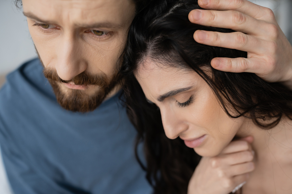 Bearded man calming and hugging displeased girlfriend at home  - 写真・画像