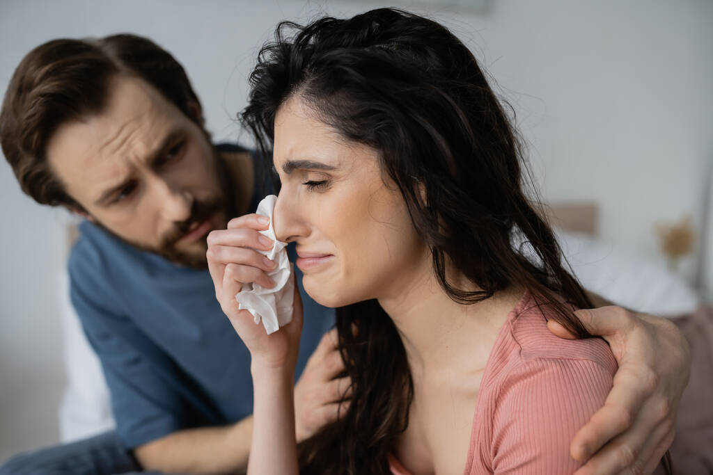 Displeased woman crying near caring blurred boyfriend at home  - Photo, Image