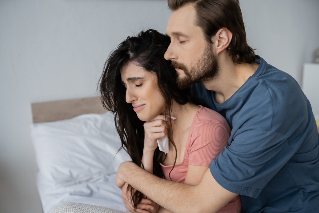 barbuto uomo abbracciare insoddisfatto fidanzata con tovagliolo in camera da letto  - Foto, immagini