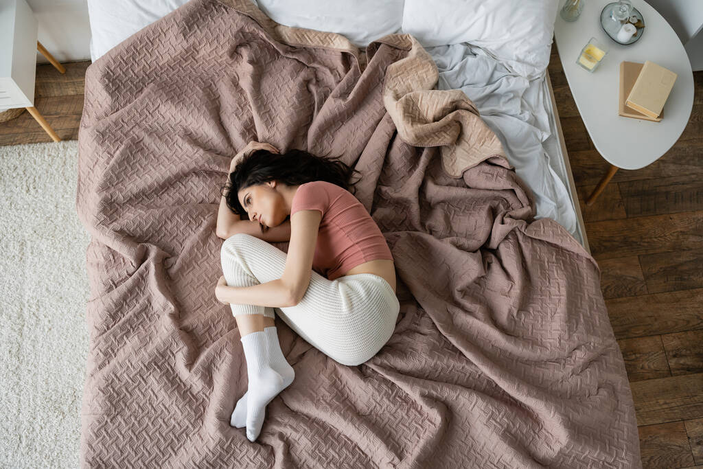 Vista superior de la mujer deprimida en pijama acostada en la cama en casa  - Foto, Imagen