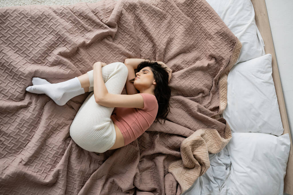 Vista dall'alto della donna sola in pigiama sdraiata sul letto a casa  - Foto, immagini