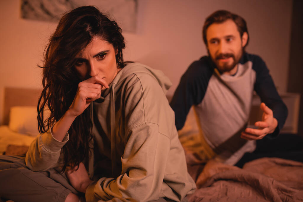 Разочарованная женщина, сидящая рядом с парнем, ссорящаяся в спальне вечером  - Фото, изображение