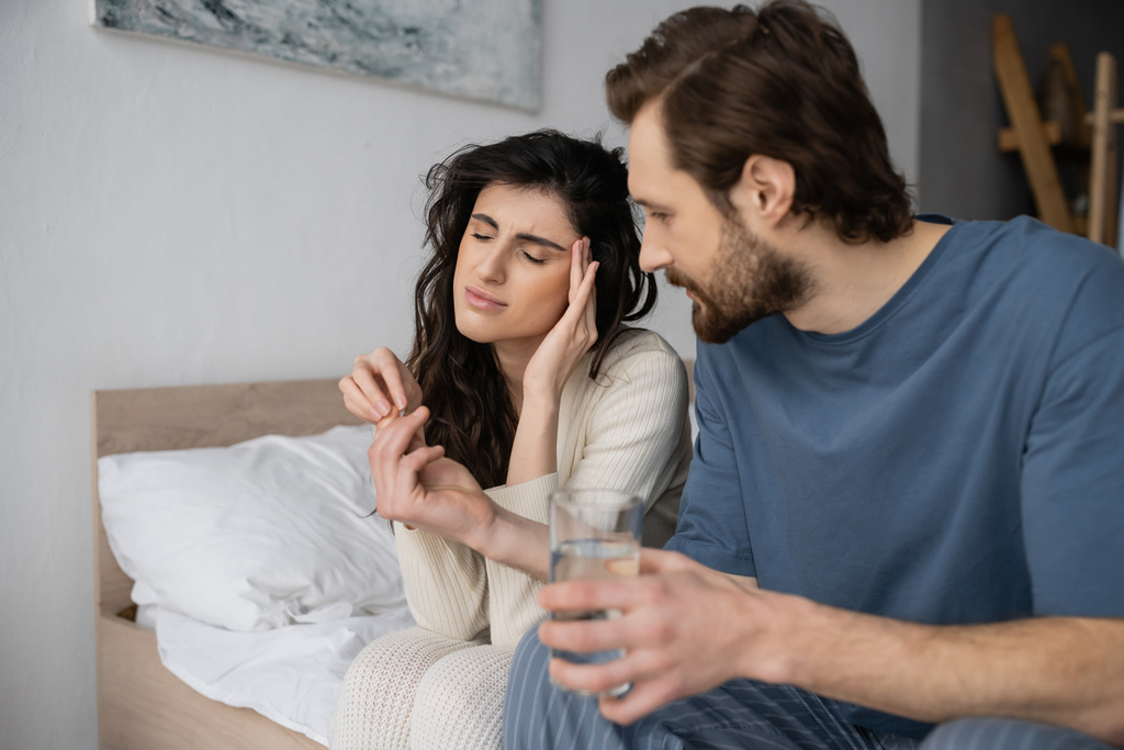 Huolehtiva mies antaa pillereitä ja vettä tyttöystävä migreeni makuuhuoneessa  - Valokuva, kuva