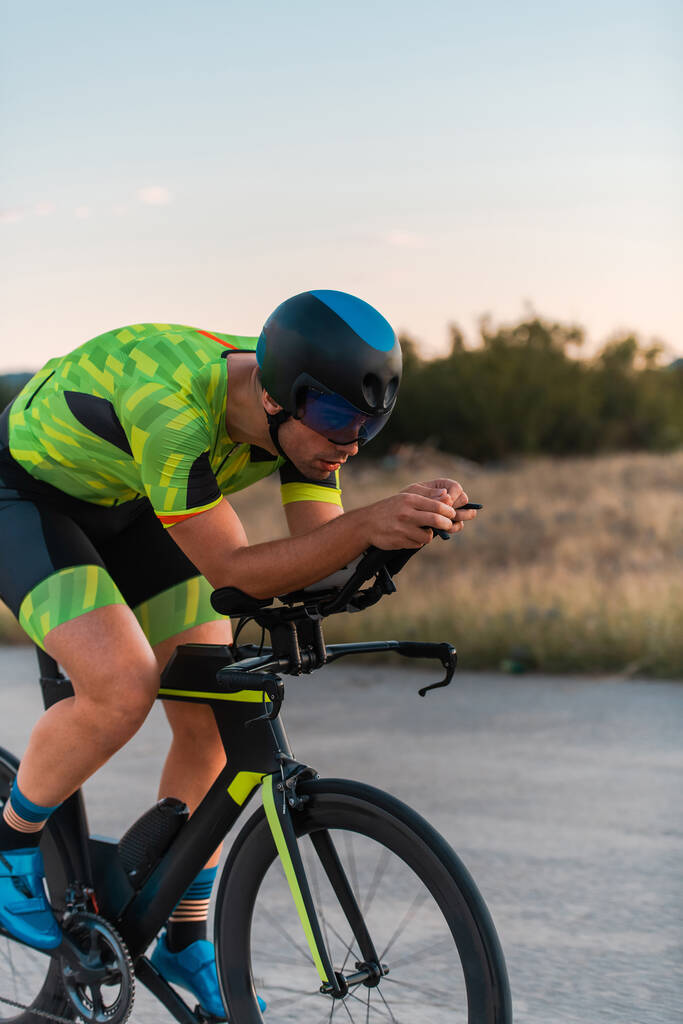  Τριαθλητής ιππεύει το ποδήλατό του το ηλιοβασίλεμα, προετοιμάζεται για μαραθώνιο. Τα ζεστά χρώματα του ουρανού παρέχουν ένα όμορφο σκηνικό για την αποφασιστική και εστιασμένη προσπάθειά του - Φωτογραφία, εικόνα