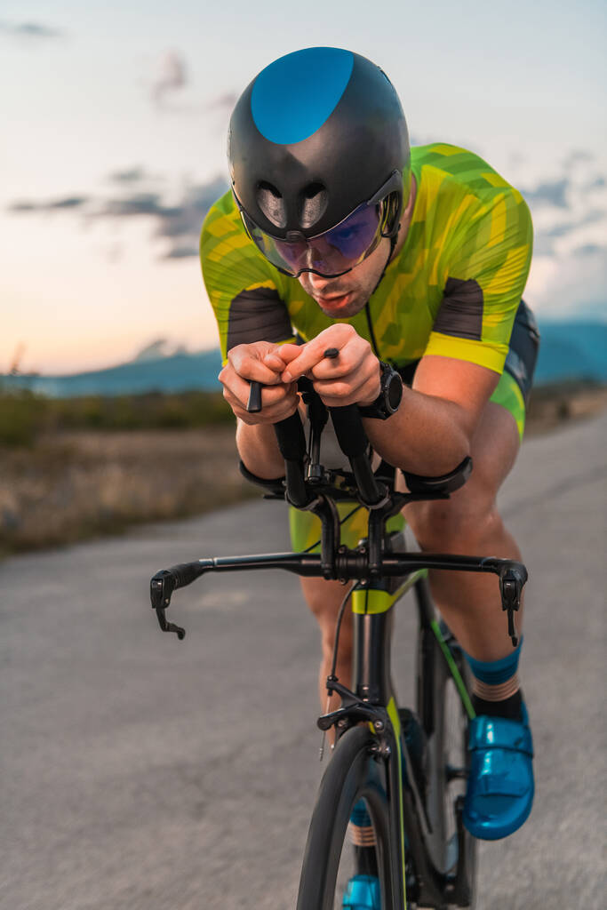  トライアスリートは日没時に自転車に乗り、マラソンの準備をする。暖かい空の色は、彼の決定的かつ集中的な努力のための美しい背景を提供します - 写真・画像