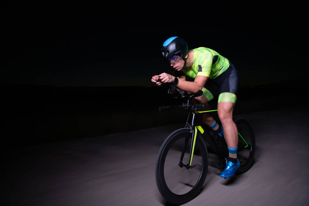 Un triatleta guida la sua moto nel buio della notte, spingendosi a prepararsi per una maratona. Il contrasto tra il buio e la luce della sua moto crea un senso di dramma e mette in evidenza il - Foto, immagini