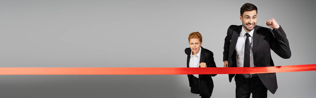 excited businessman showing triumph gesture near finish ribbon and upset woman running on grey background, banner - Photo, Image