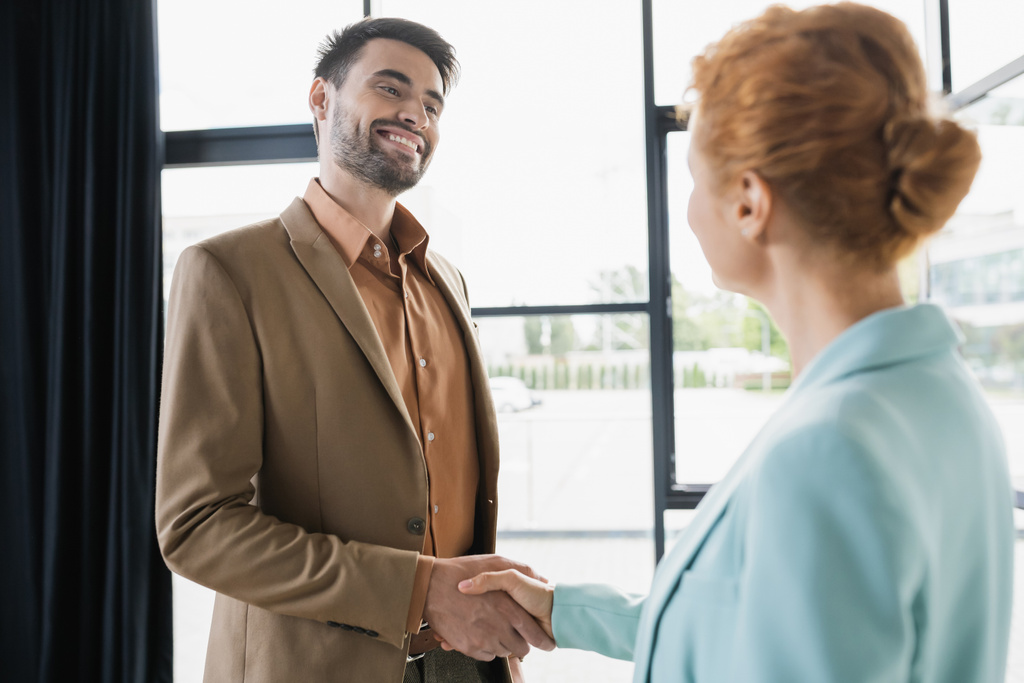 successful businessman smiling and shaking hands with redhead woman in office - Photo, Image
