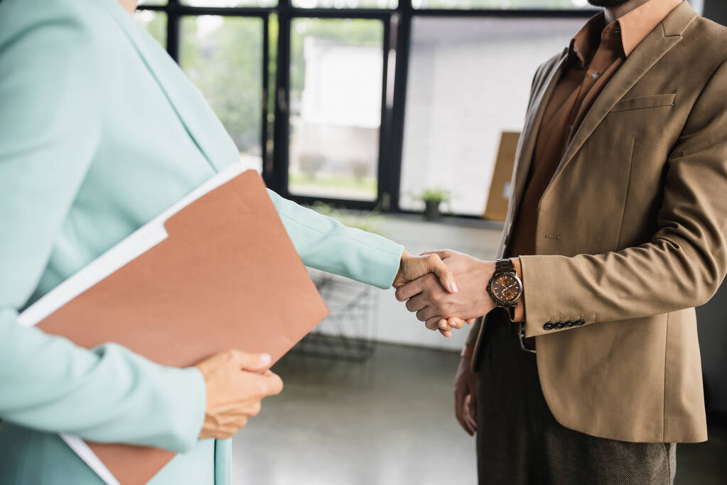 Ausgeschnittener Blick auf Geschäftsfrau mit Ordner beim Händeschütteln mit Büropartnerin - Foto, Bild