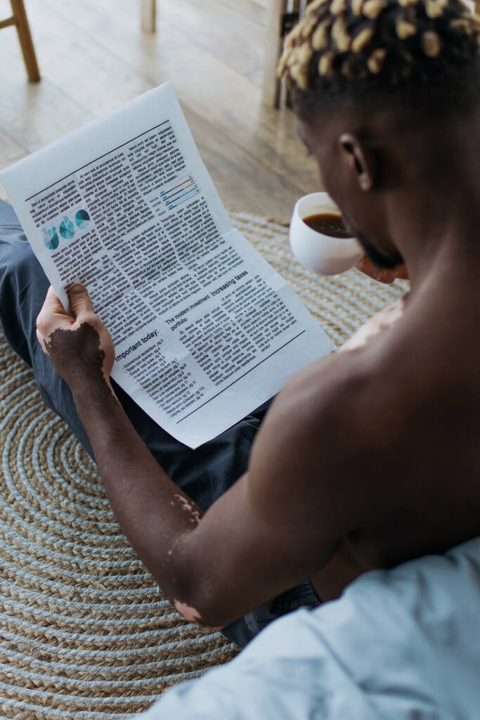 Безсоромний афроамериканець з вітиліго читає газету і п "є каву вдома.  - Фото, зображення