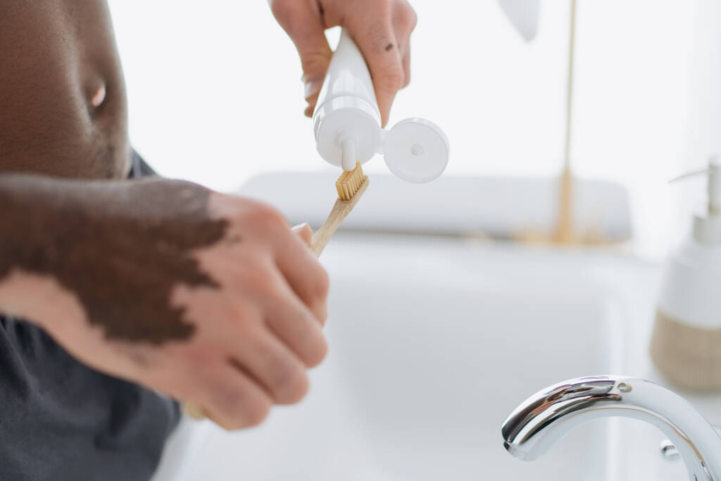 Προβολή του Αφροαμερικανού με λεύκη να πιέζει οδοντόκρεμα στην οδοντόβουρτσα στο μπάνιο  - Φωτογραφία, εικόνα