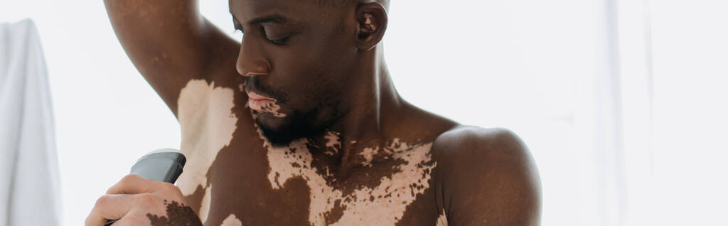 Homme afro-américain avec vitiligo tenant déodorant dans la salle de bain, bannière  - Photo, image