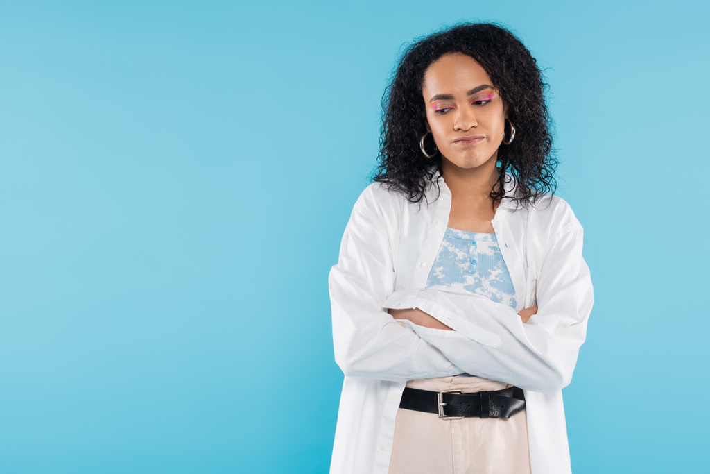 засмучена афроамериканська жінка в білій сорочці зі складеними руками ізольованими на синьому - Фото, зображення