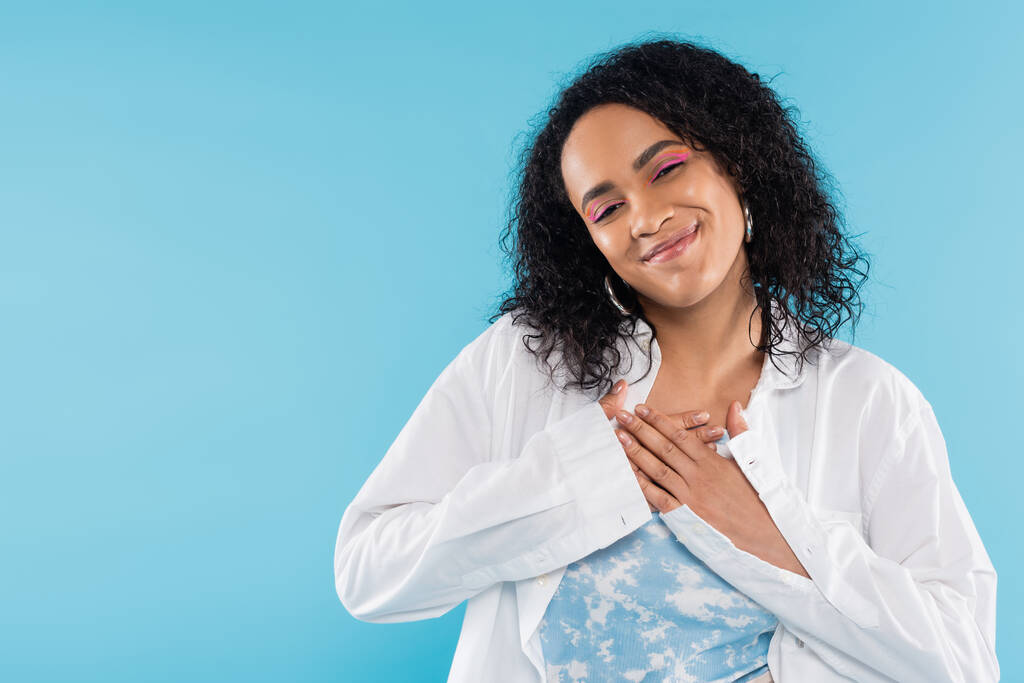 pleased african american woman touching chest and smiling at camera isolated on blue - Photo, Image