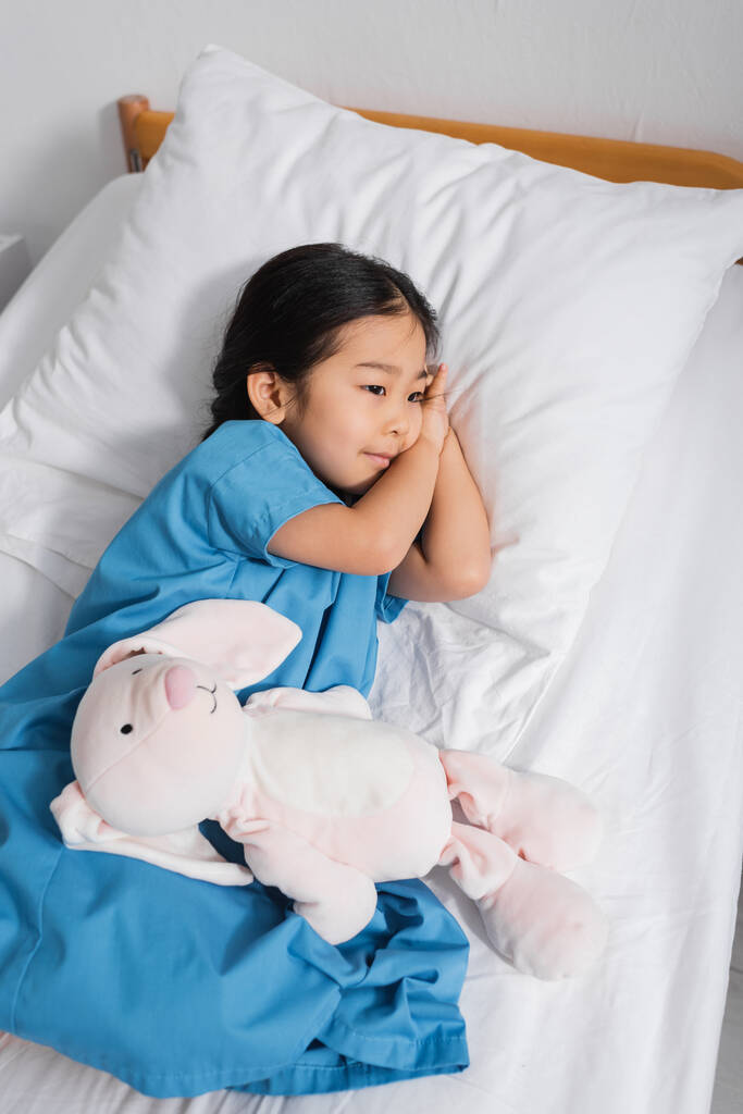 vue grand angle de rêve asiatique enfant couché sur lit d'hôpital près de jouet lapin et regarder loin - Photo, image