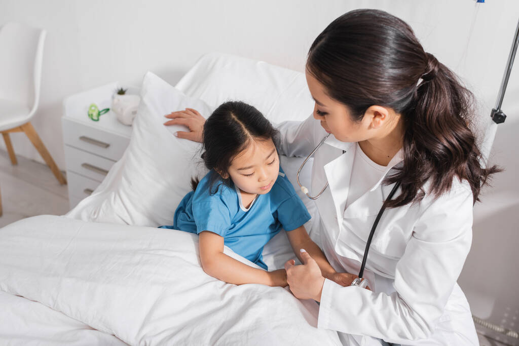 цікава азіатська дитина торкається стетоскопа біля лікаря на ліжку в лікарні
  - Фото, зображення