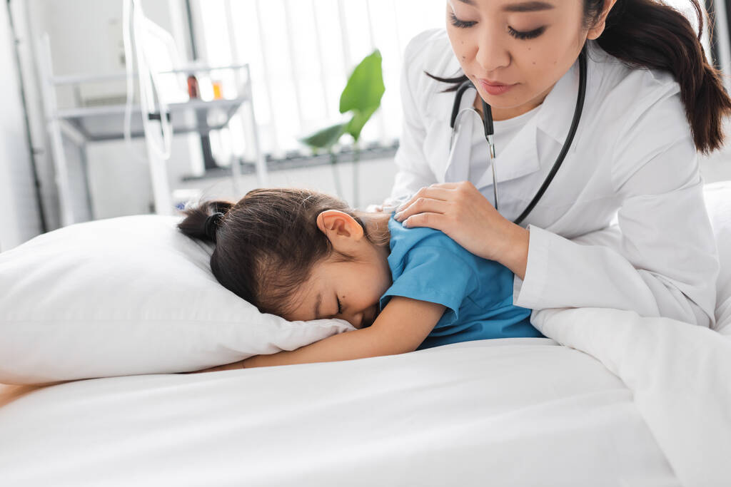 aasialainen lääkäri rauhoittava masentunut lapsi peittää kasvot tyyny sairaalassa sängyssä - Valokuva, kuva