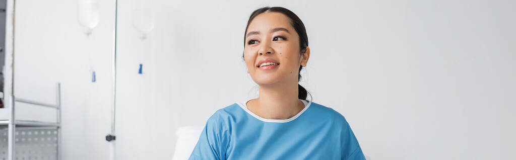 mladá Asiatka v nemocničním plášti s úsměvem a pohledem upřeným na kliniku, banner - Fotografie, Obrázek