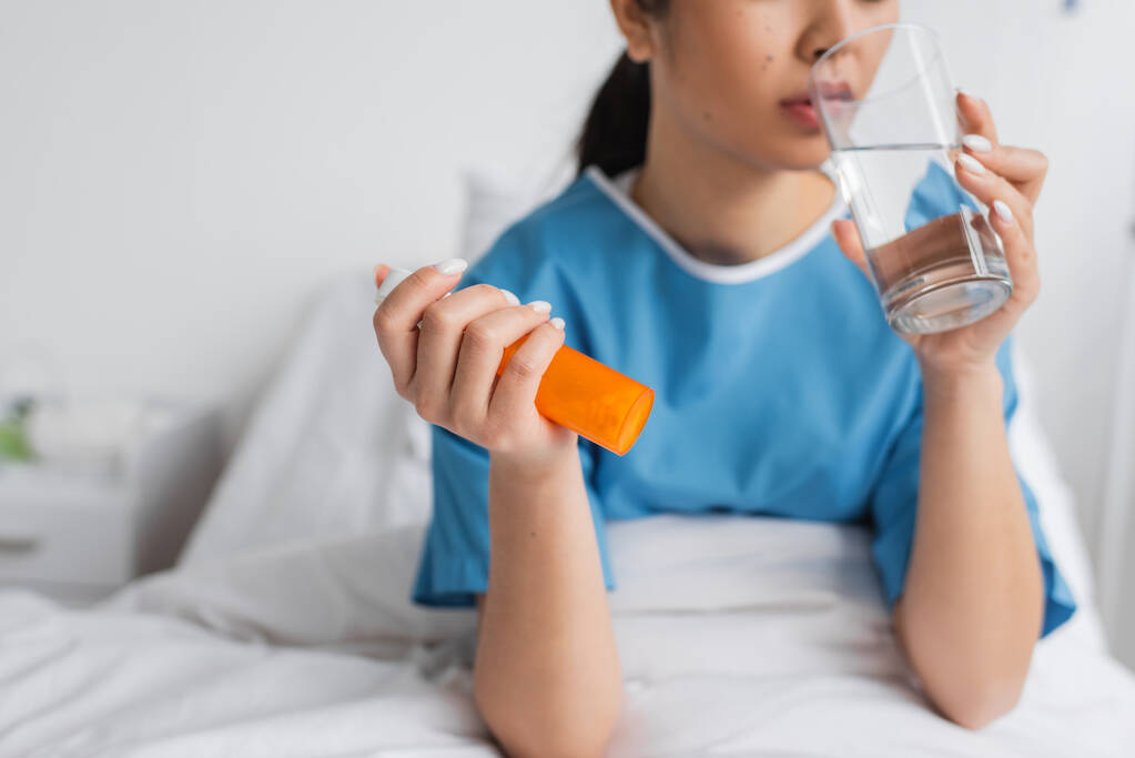częściowy widok chorej kobiety trzymającej pojemnik z tabletkami i wodę pitną na oddziale szpitalnym - Zdjęcie, obraz