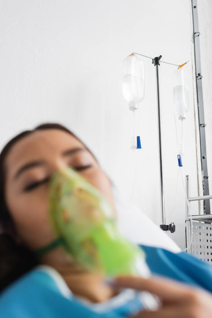 desfocado ásia mulher com fechado olhos respirando no oxigênio máscara no hospital ward - Foto, Imagem