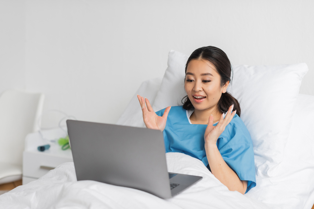 erstaunt asiatische Frau zeigt wow Geste während Videoanruf auf Laptop auf Krankenhausbett - Foto, Bild