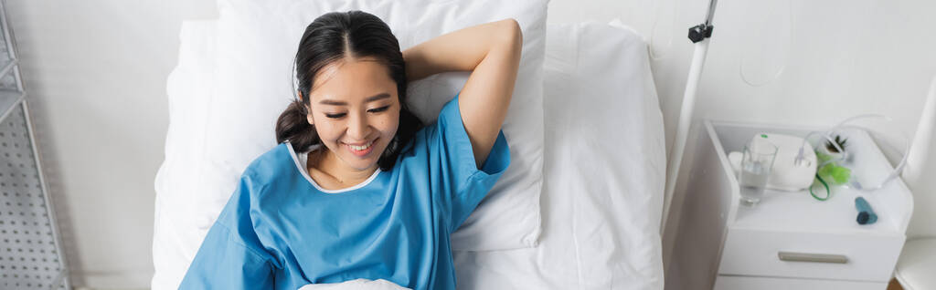 młoda Azjatka w szpitalnej sukni uśmiechnięta do łóżka, sztandar - Zdjęcie, obraz