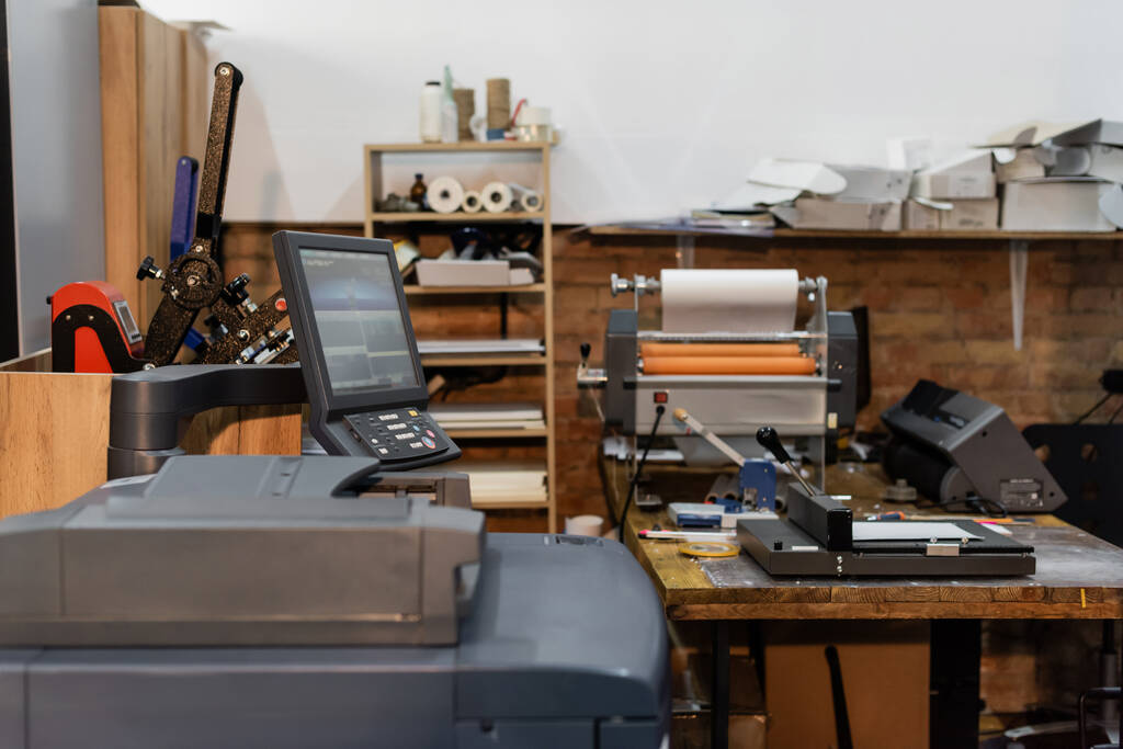 современное оборудование печатного центра рядом с монитором и триммером для бумаги  - Фото, изображение