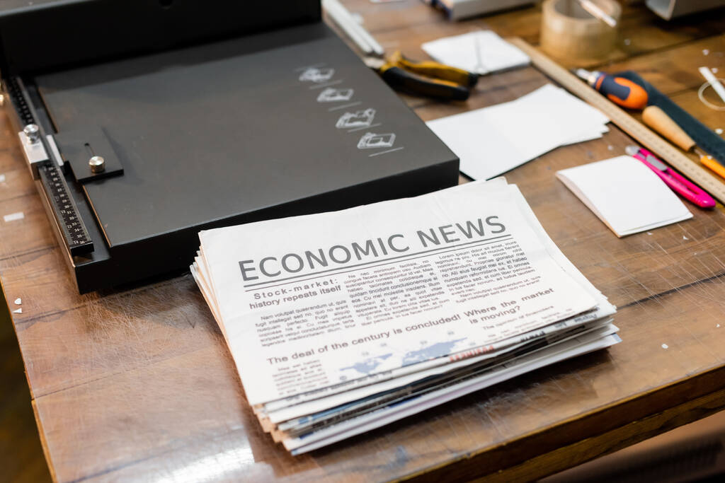 visão de alto ângulo de jornais com notícias econômicas perto de máquina de aparador de papel profissional  - Foto, Imagem