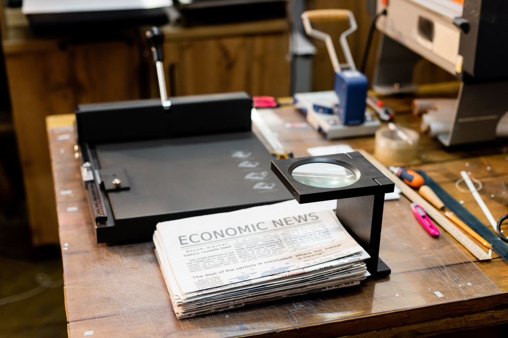 μεγεθυντικός φακός πάνω από εφημερίδες με οικονομικές ειδήσεις και επαγγελματική μηχανή κουρέματος χαρτιού  - Φωτογραφία, εικόνα