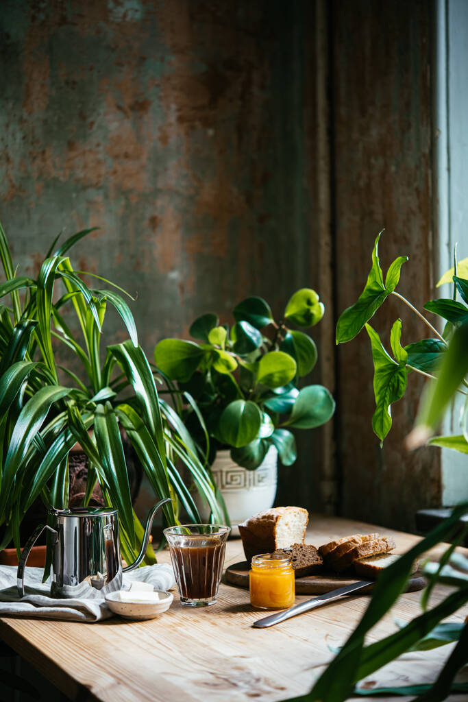 Πρωινό με κρουασάν και καφέ σερβίρεται σε ένα όμορφο τραπέζι γεμάτο φυτά. Απολαμβάνοντας το χρόνο στο σπίτι έννοια. - Φωτογραφία, εικόνα