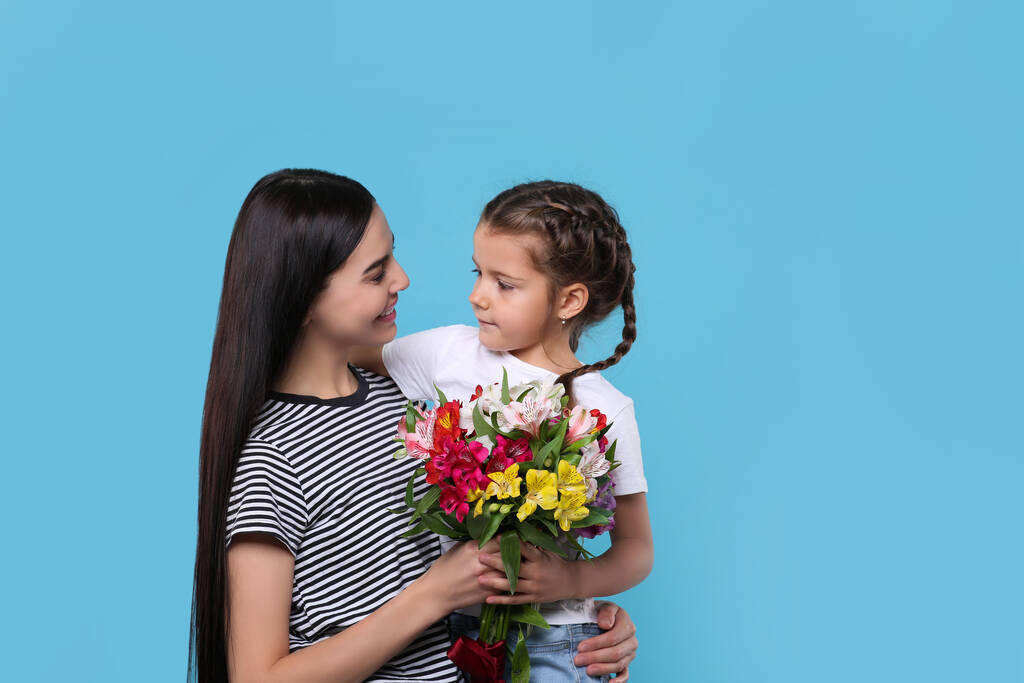 Szczęśliwa kobieta z córką i bukiet pięknych kwiatów na jasnoniebieskim tle, miejsce na tekst. Święto Dnia Matki - Zdjęcie, obraz