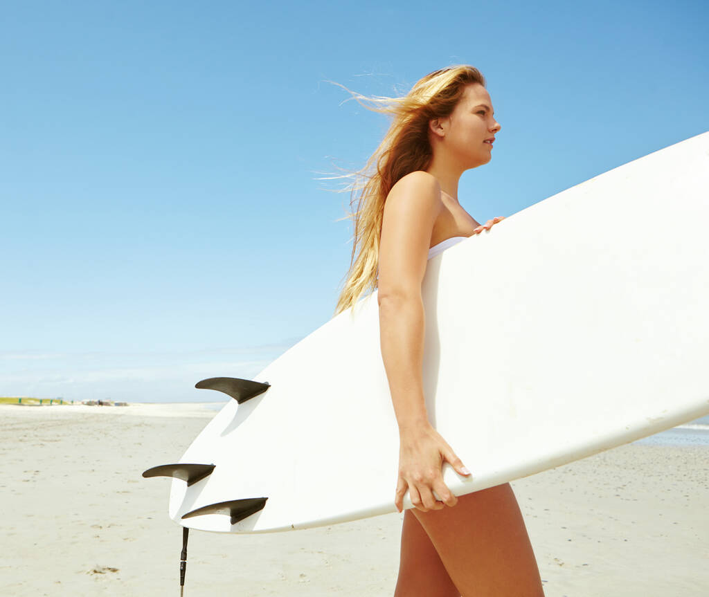 Surfer beauté. une jeune surfeuse portant sa planche de surf sur la plage - Photo, image