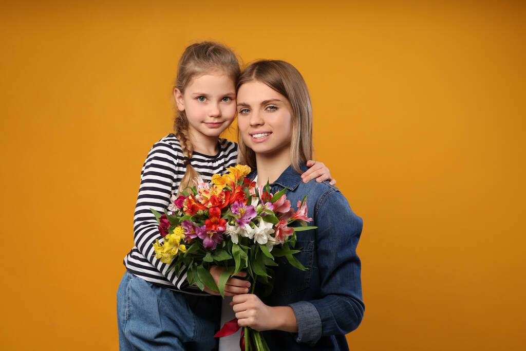 Hijita felicitando a su madre con flores sobre fondo naranja. Feliz Día de la Madre - Foto, imagen