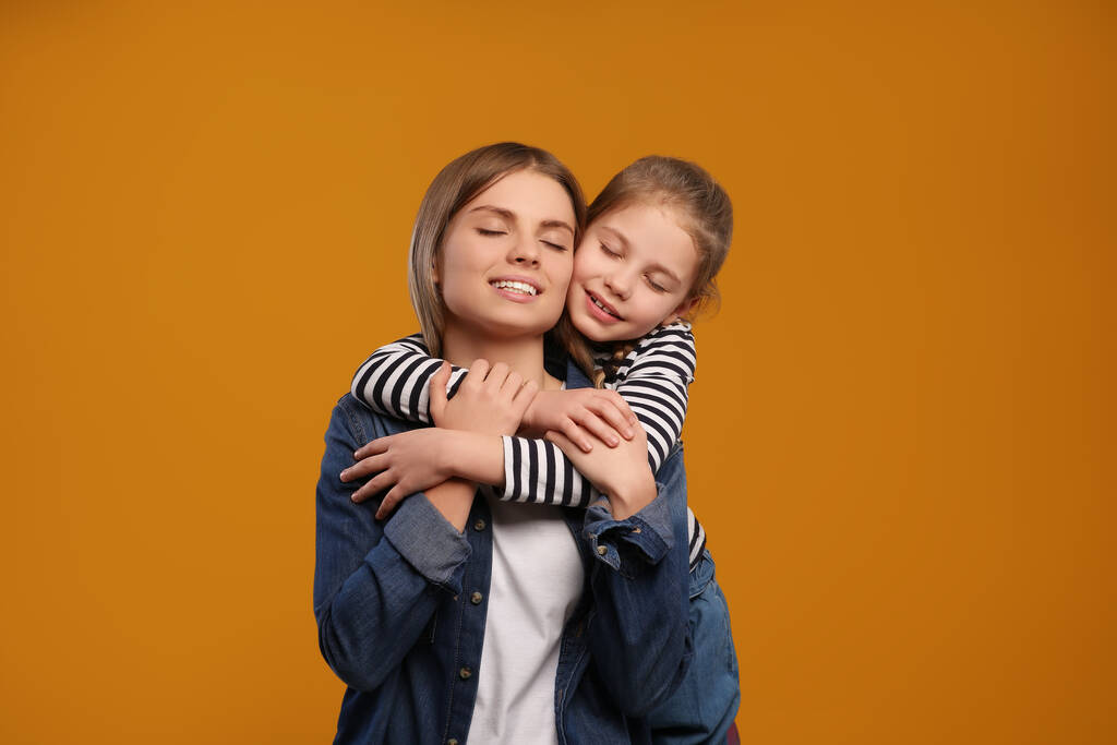Kleine dochter knuffelt haar moeder op oranje achtergrond. Gelukkige Moederdag - Foto, afbeelding